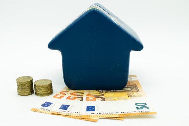 Pequena casa em pé sobre moedas de euro fica ao lado dela em um fundo branco