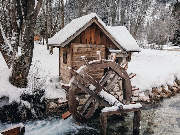 Pequeña casa de madera y rueda de molino arroyo nieve de invierno