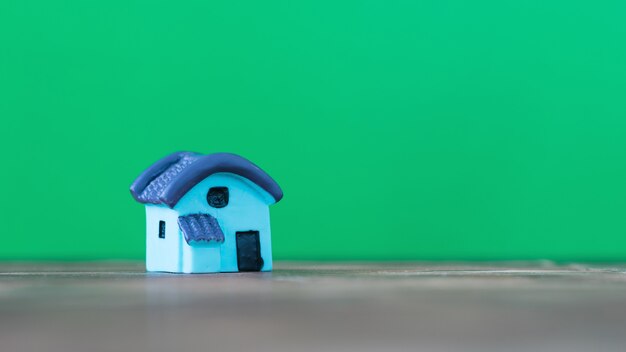 Pequeña casa en miniatura con techo azul sobre una mesa de madera con una superficie verde