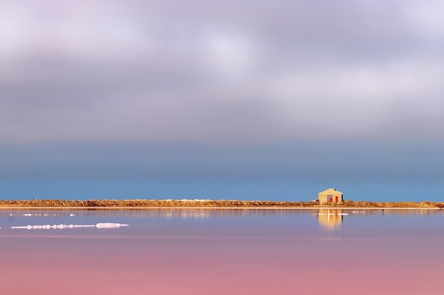 Una pequeña casa de piedra abandonada se encuentra en un lago salado rosa bajo un cielo azul brillante