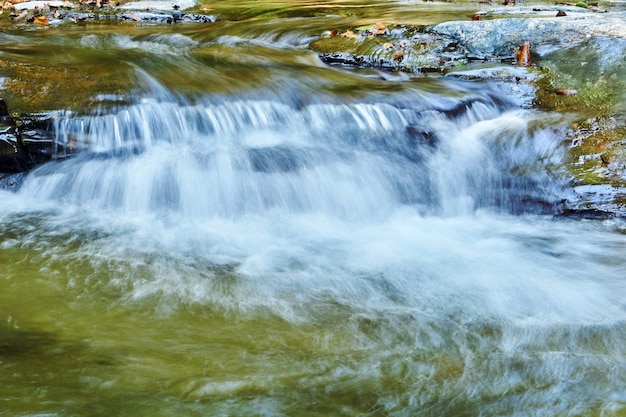 Pequeña cascada en un arroyo de montaña entre rocas, los chorros de agua se difuminan en movimiento