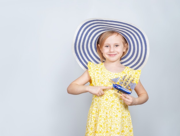 Una pequeña caucásica con un sombrero de ala ancha señala con el dedo un bote de juguete. El concepto de vacaciones de verano.