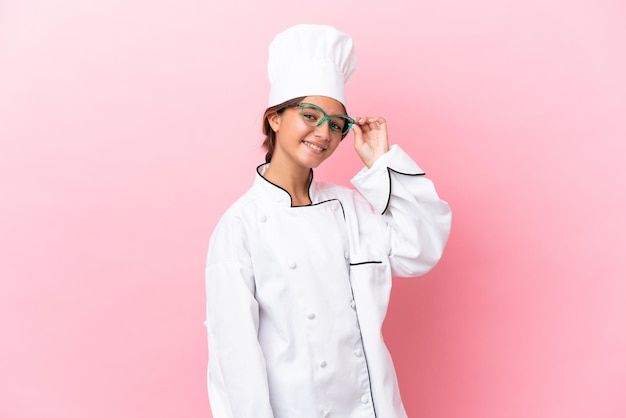 Foto pequena chef caucasiana isolada em fundo rosa com óculos e feliz