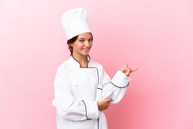 Foto pequena chef caucasiana isolada no fundo rosa, apontando o dedo para o lado