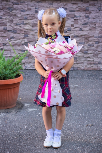 Foto pequeña colegiala con flores de primer grado en uniforme