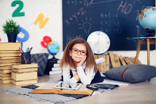 Pequeña colegiala inteligente con tableta digital en un aula.