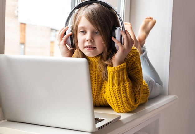 Pequeña colegiala linda que usa la computadora portátil en casa se comunica en Internet