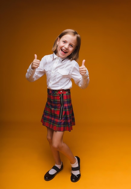 Una pequeña colegiala muestra un gesto de aprobación de la clase con ambas manos aisladas en un fondo amarillo