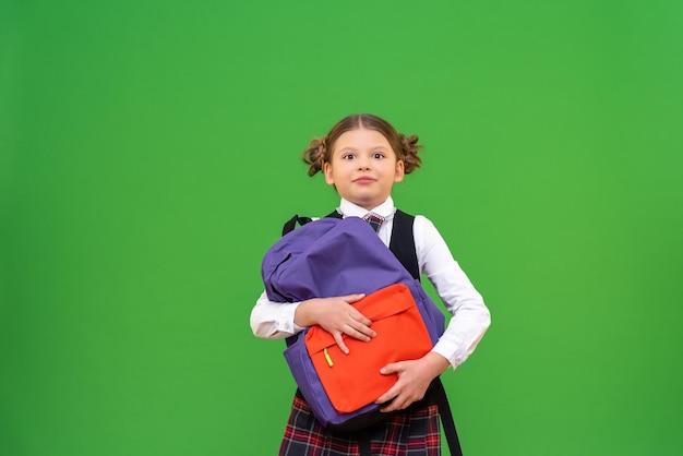 Una pequeña colegiala sostiene un maletín pesado con libros de texto.