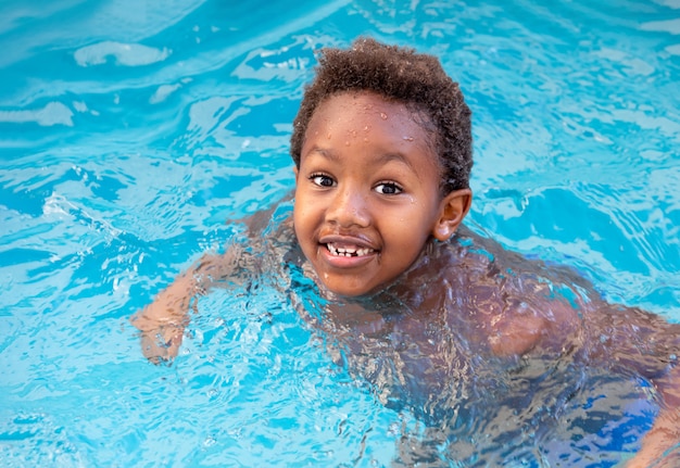 Pequena criança africana espirrando na piscina