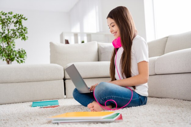 pequeña dama de ensueño usar auriculares relajarse sentarse alfombra con la computadora portátil en las rodillas