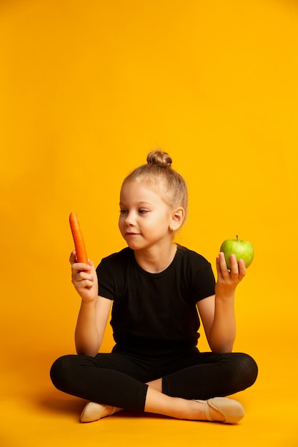 Pequena dançarina confusa escolhendo entre cenoura e maçã verde