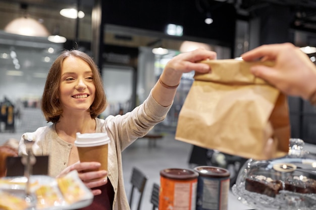 pequena empresa, comida para viagem, pessoas e conceito de serviço - cliente do sexo feminino feliz com xícara de café levando saco de papel do homem ou barman no café vegan