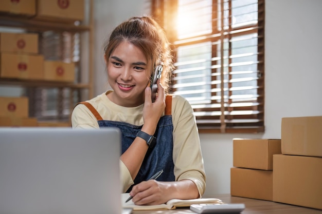 Foto pequena empresa empreendedora pme mulher freelancer usando uma chamada telefônica recebida de um cliente verificando o produto em estoque no escritório em casa marketing on-line embalagem caixa de entrega conceito de comércio eletrônico pme