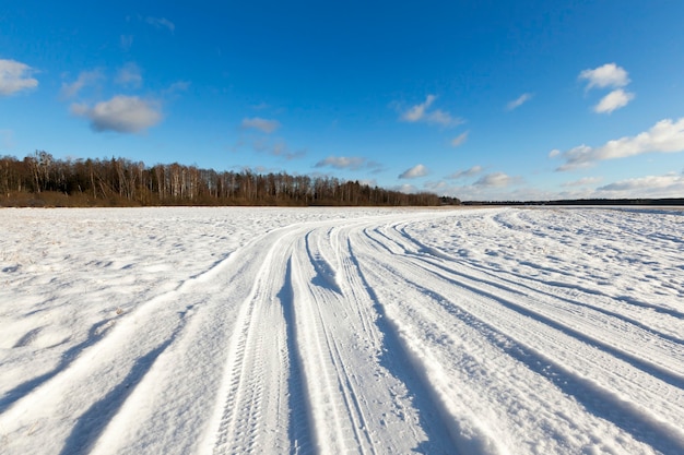 Pequena estrada no inverno com sulcos de pneus de carros. no terreno há neve após queda de neve. céu azul ao fundo