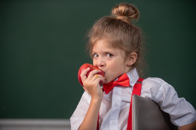 Pequena estudante estudante na classe comendo maçã na escola Crianças engraçadas encaram de perto