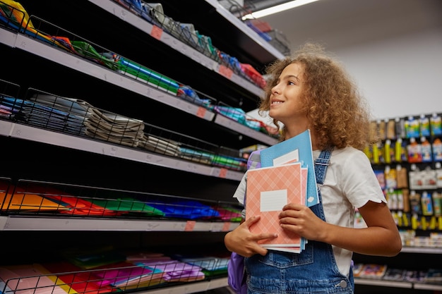 Foto pequena estudante selecionando e comprando cadernos em uma loja de artigos de papelaria