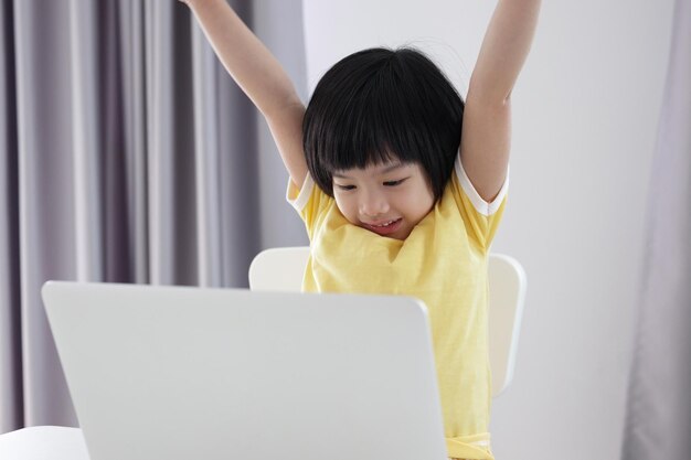 Una pequeña estudiante asiática estudia en línea usando una computadora portátil en casa