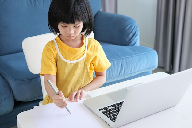 Una pequeña estudiante asiática estudia en línea usando una computadora portátil en casa