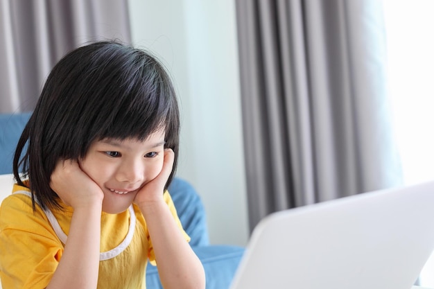 Una pequeña estudiante asiática estudia en línea usando una computadora portátil en casa