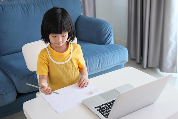 Una pequeña estudiante asiática estudia en línea usando una computadora portátil en casa