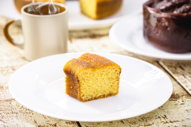 Pequena fatia de bolo de fubá, típico bolo rural brasileiro feito com farinha de milho, com café quente ao fundo, goiabada ao fundo com queijo