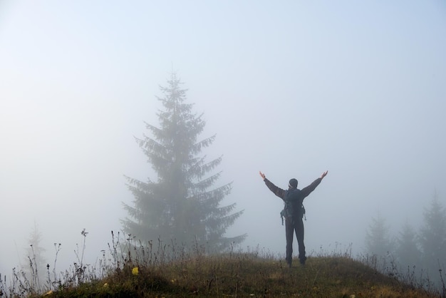 Pequeña figura de excursionista solitario disfrutando de su tiempo en el sendero del bosque salvaje en el día de otoño brumoso