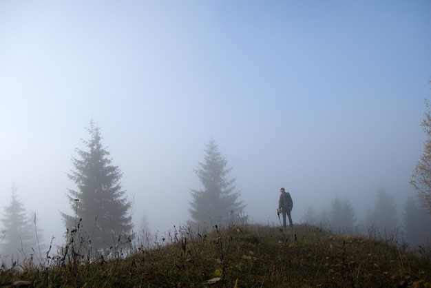 Pequeña figura de excursionista solitario disfrutando de su tiempo en el sendero del bosque salvaje en el día de otoño brumoso