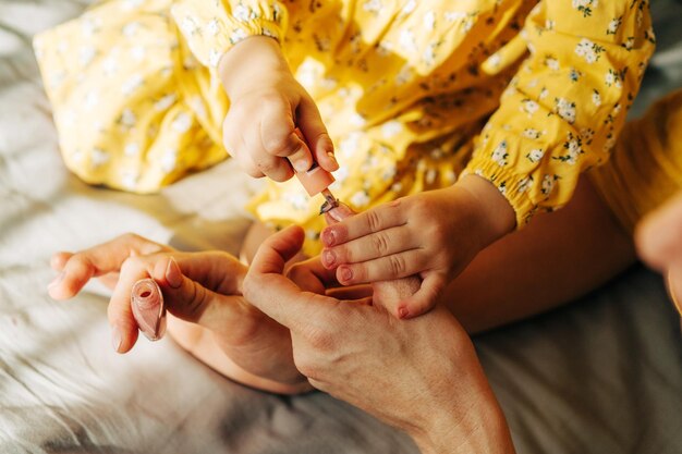 Foto pequena filha irreconhecível pinta as unhas de sua mãe com esmalte