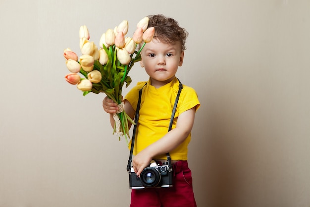 Pequena fotógrafa, uma criança com uma câmera em suas mãos e flores. buquê de tulipas para o dia das mães.