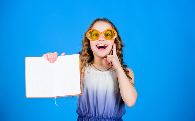 Pequena garota feliz de óculos com notebook fazendo planos para férias de verão e férias pequena garota de beleza escreve suas memórias notas de diário lendo livro Moda de verão olha o que eu tenho espaço de cópia