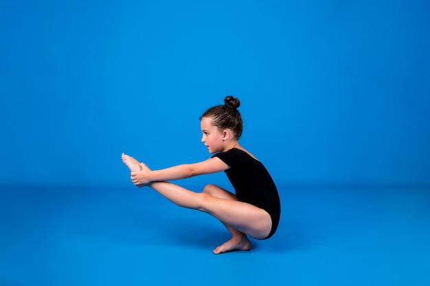 Una pequeña gimnasta enfocada realiza un ejercicio de equilibrio sobre un fondo azul con un lugar para el texto