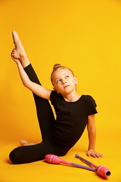 Pequeña gimnasta estirando la pierna cerca de las varitas durante el entrenamiento