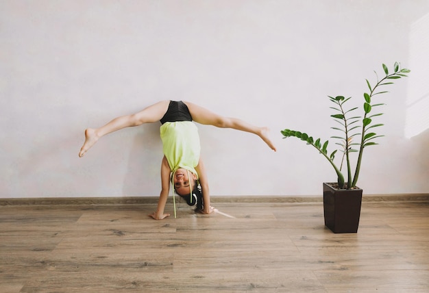 Pequena ginasta faz exercícios em casa garota fazendo exercício perto da parede