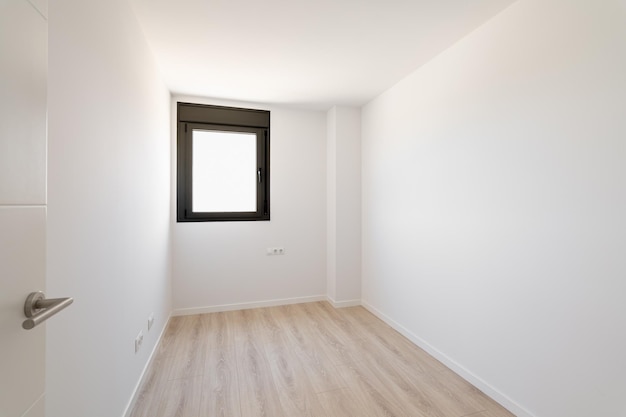 Pequeña habitación vacía sin muebles el piso es nuevo laminado de madera clara una ventana hecha de negro