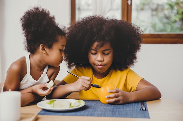 Pequeña hermana menor linda que parece interesante, su hermana mayor intenta aprender a comer vegetales.