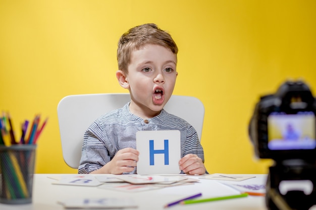 Foto pequeña y hermosa bloguera que escribe sobre cómo aprender el alfabeto en amarillo. de vuelta a la escuela. educación en línea a distancia.