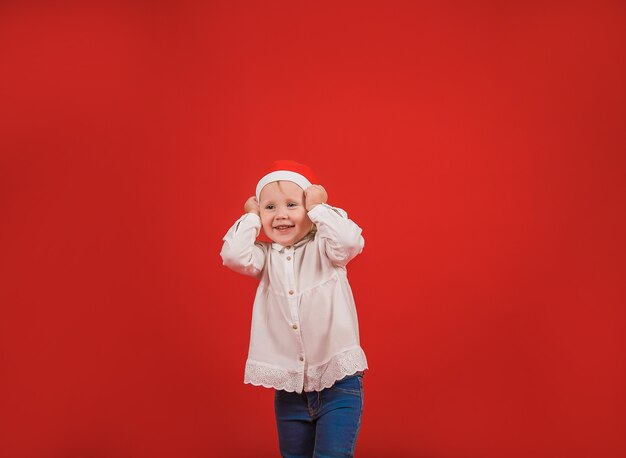 Pequeña hermosa niña feliz está de pie sobre un fondo rojo en un sombrero de Año Nuevo sonriendo