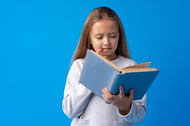 Pequeña y hermosa niña sonriente sosteniendo un libro contra el fondo azul.