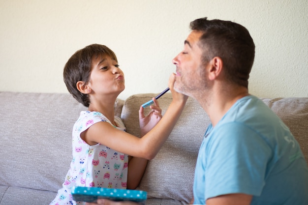 Pequeña hija linda haciendo maquillaje a su padre