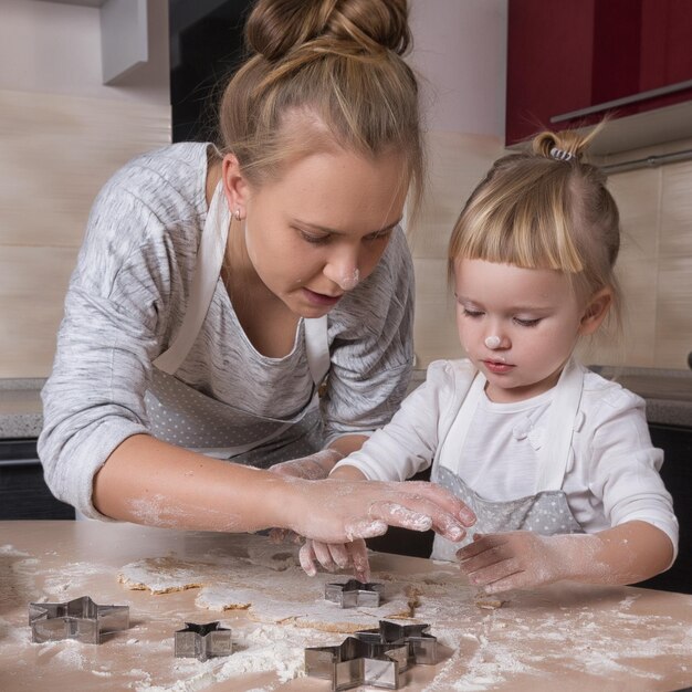 Una pequeña hija pasa tiempo con su madre en la cocina para hornear galletas.