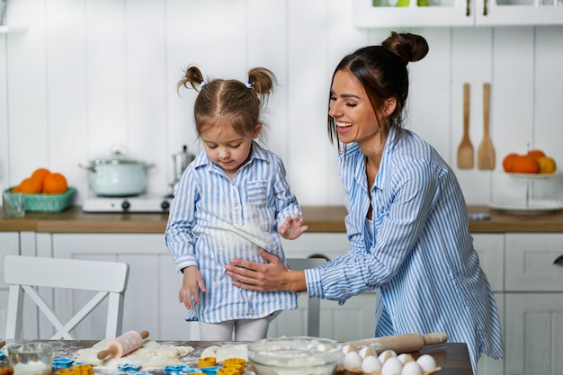 Pequeña hija que ayuda a su madre que cocina galletas durante las vacaciones.