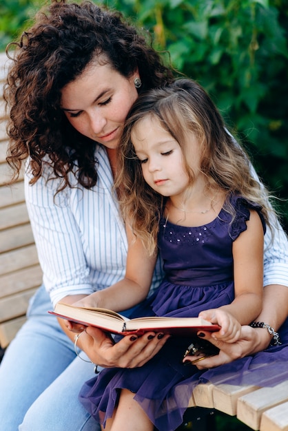 Una pequeña hija y su madre están sentadas en un banco en el parque, leyendo un libro interesante