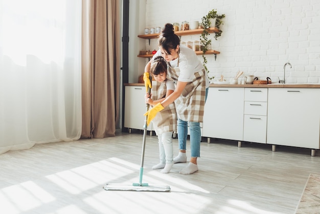 Una pequeña hija y su mamá limpian la casa un niño lava el piso de la cocina una linda niña ayudante limpia el piso con un trapeador una familia feliz limpia la habitación