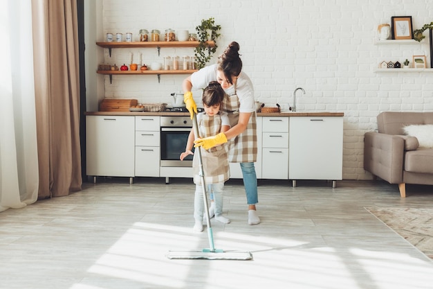 Una pequeña hija y su mamá limpian la casa un niño lava el piso de la cocina una linda niña ayudante limpia el piso con un trapeador una familia feliz limpia la habitación