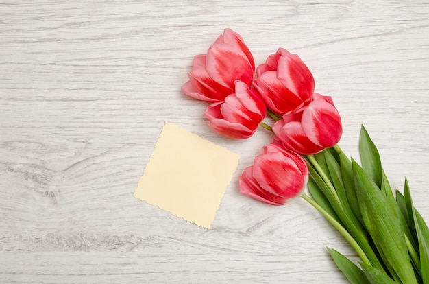 Pequeña hoja de papel en blanco y tulipanes rosados sobre un fondo de madera clara