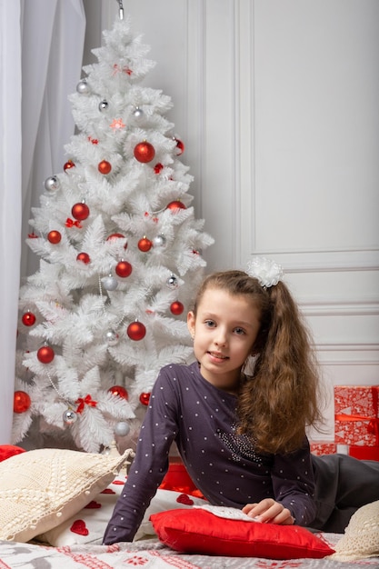 Pequena linda garota casual vestida sentada na sala branca entre as decorações de natal