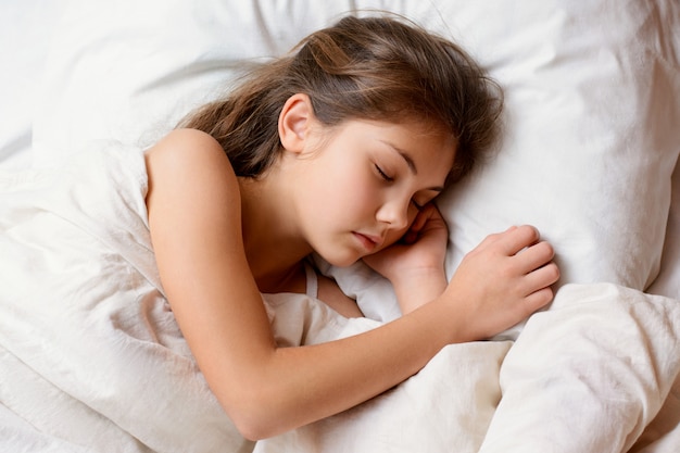 Pequena menina adorável encontra-se na cama confortável, tendo bons sonhos agradáveis, descansando após um dia duro de estudar na escola