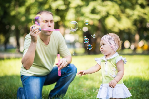 Pequena menina andando com o pai e tentando pegar bolhas