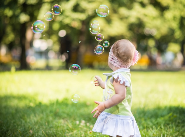 Pequena menina andando na grama e tentando pegar bolhas